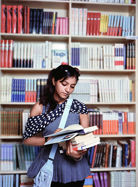 Portrait of a beautiful Indian /Asian girl / female student reading a book in the library campus.