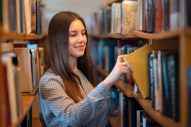 young-smiling-girl-standing-near-bookshelves-library-taking-books-reading-literature-lesson-science-research-education-getting-knowledge-university-concept_123211-6387